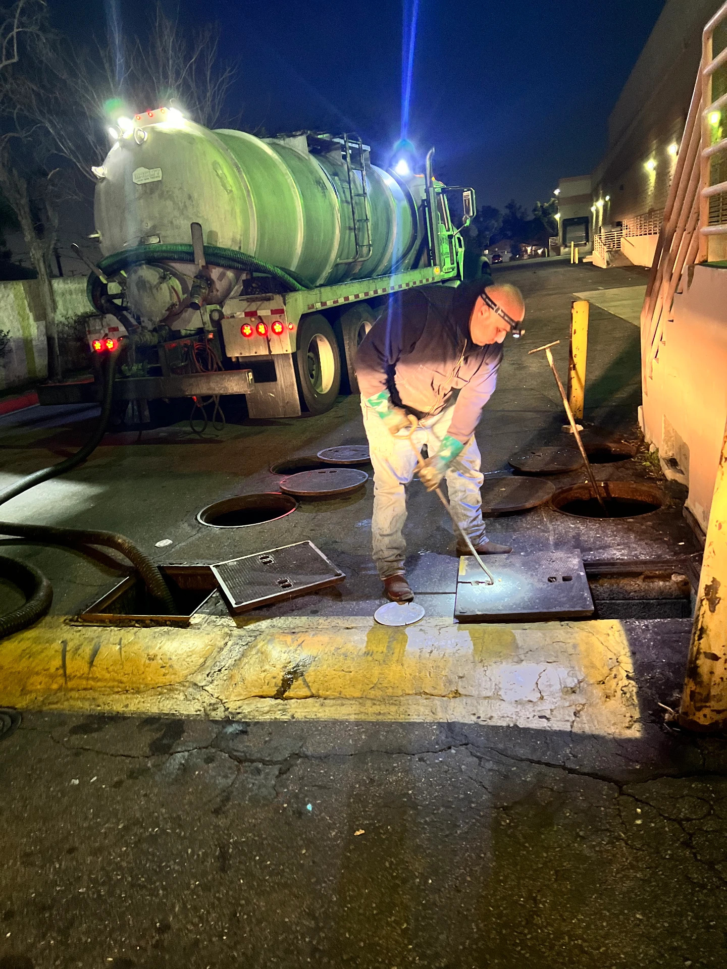 Night crew opening grease interceptor lids beside a vacuum truck in Eastvale, California