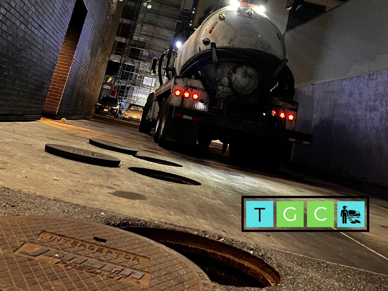 Vacuum truck pumping a grease interceptor in a restaurant alley at night in La Quinta, California